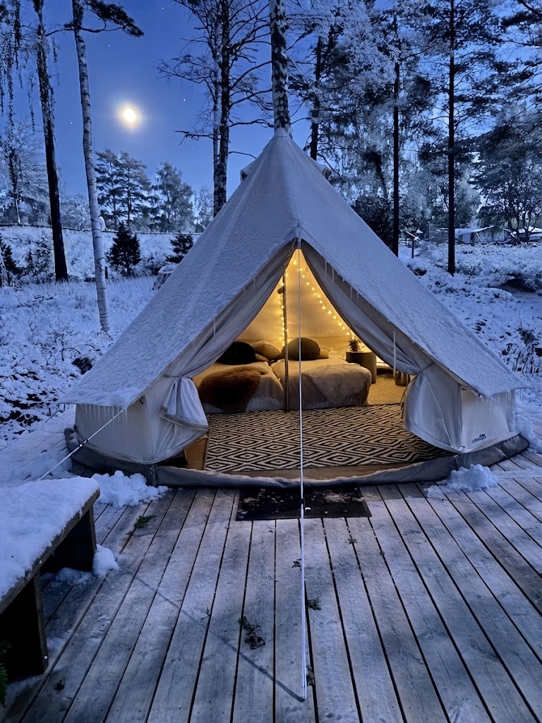 Bell tent-glampingtält på trädäck i dalaskog med snö och kvällsbelysning