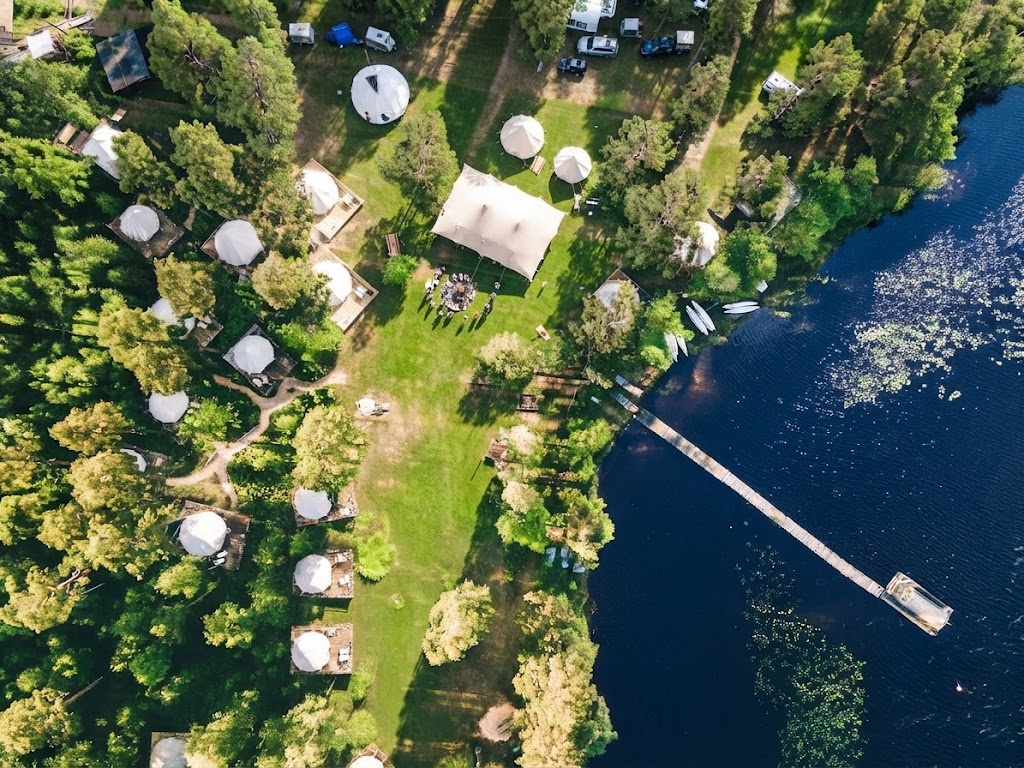 Flygvy över glamping- och campingområde vid vatten i Östergötland med tält bland träden